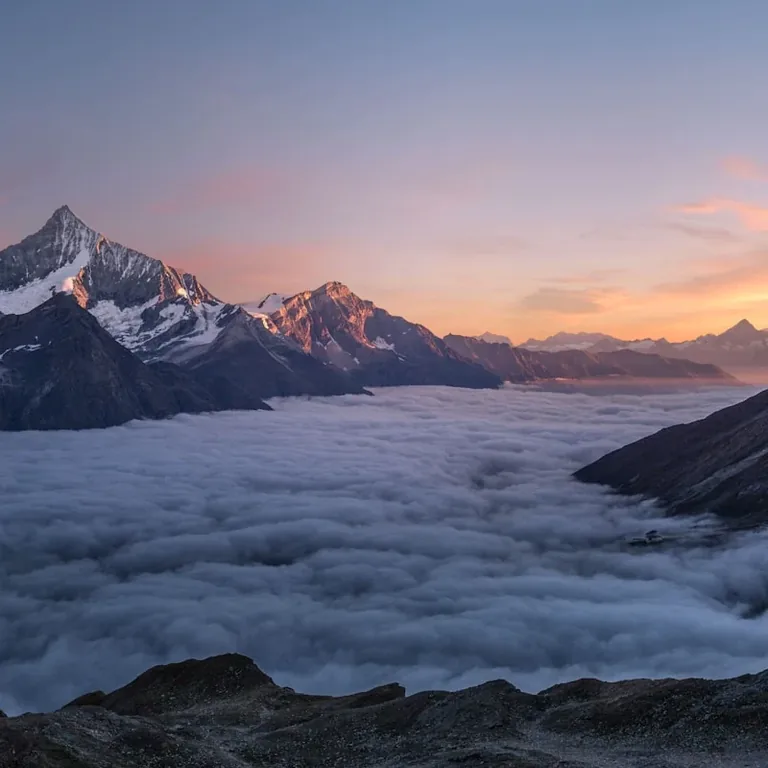 Snow peaks rising out of a sea of cloud at sunset
