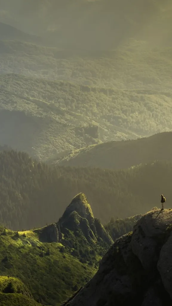 A lone figure on a green ridge in a misty mountain valley