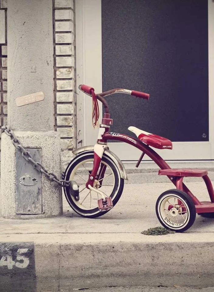 A red tricycle parked against a painted concrete wall