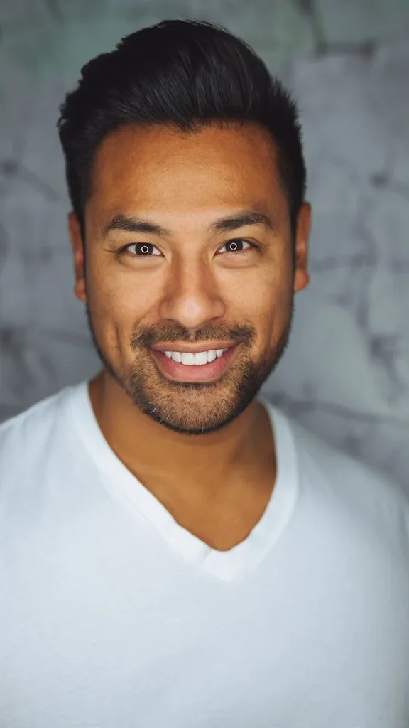A smiling man in a white t-shirt against a pale wall