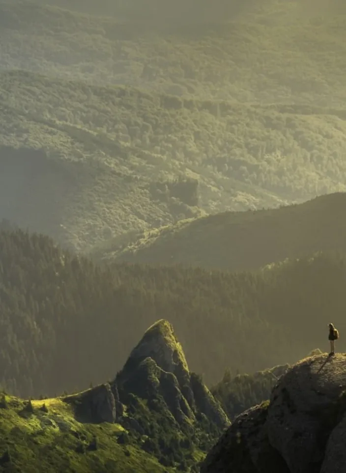 A hiker standing on a green ridge above layered mist