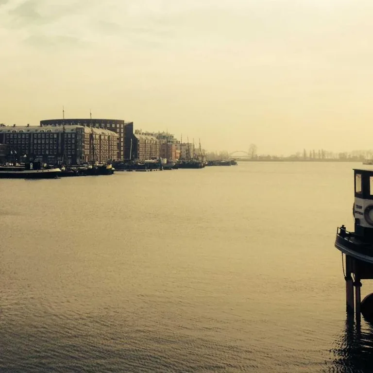 A pale city waterfront seen across still water at dawn