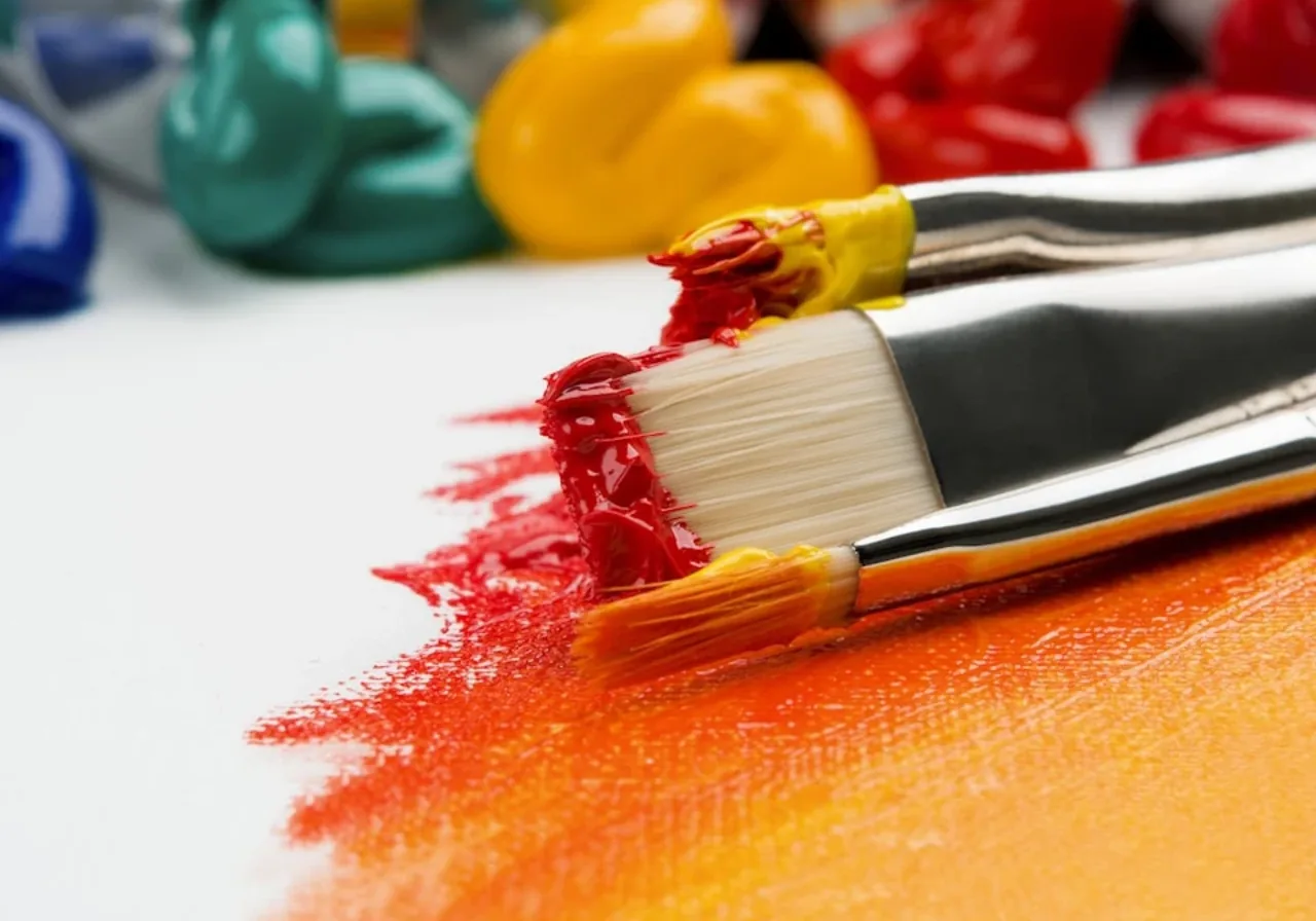 A paintbrush loaded with red paint over orange and yellow strokes