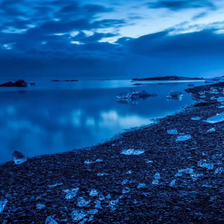 A blue night shoreline of dark rocks under a wide sky